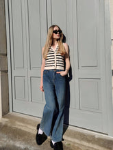 A lady wears a vest and bootcut jeans.